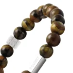 Rjava zapestnica iz sijočih okroglih kamnov (tigrovo oko) z elastičnim nizom in kovinskim detajlom z napisom “ROCHET”.